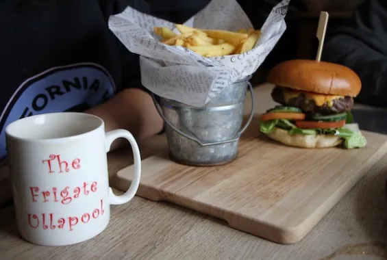 Burger and a bucket of chips on a wooden board beside a Frigate Ullapool mug